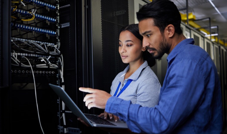 Two IT analysts examining a laptop in a server room